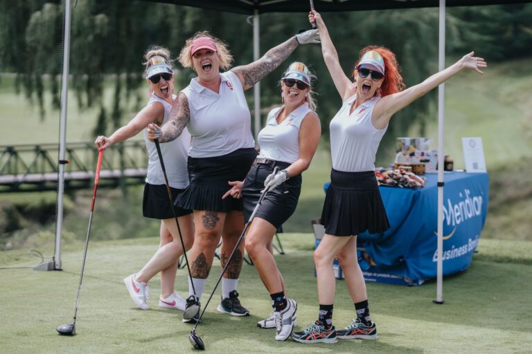 Four Wise Girls golfers in white tops cheering with clubs raised on the tee