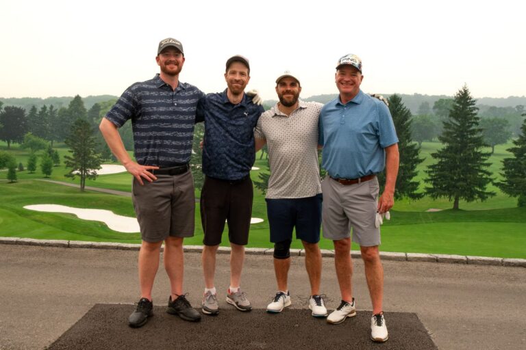 Foursome posing on the tee with the course behind them